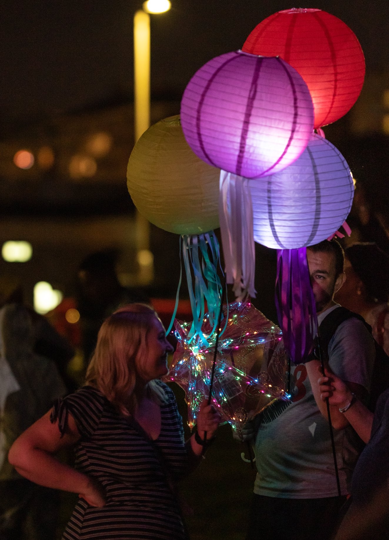 Parade participants carry colorful paper lanterns through the evening