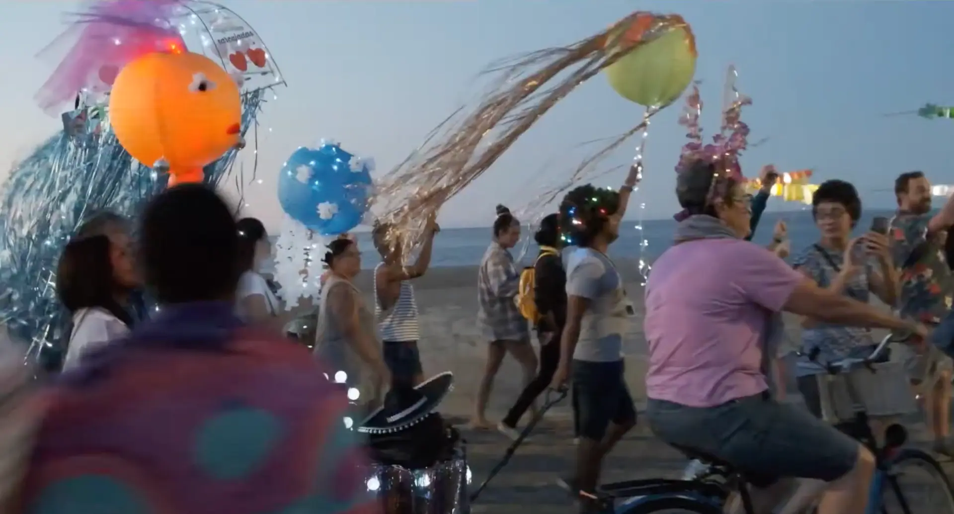 Colorful fish and balloon lanterns move along the waterfront at dusk