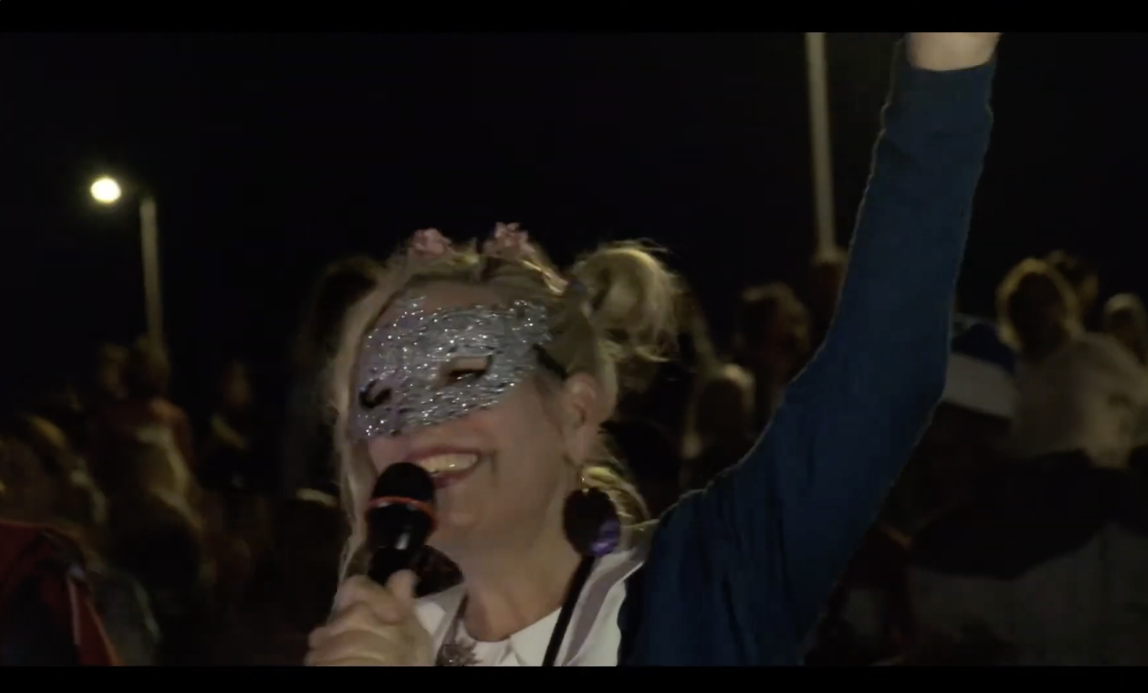 A parade host in a sparkling silver mask speaks into a microphone at the night parade